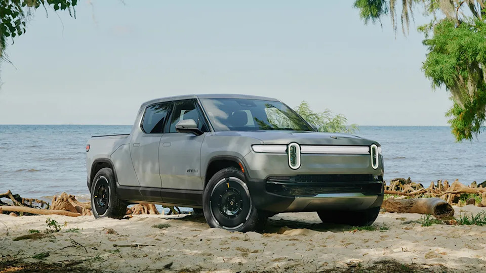 A white Rivian R1T near a beach, front 3/4 view