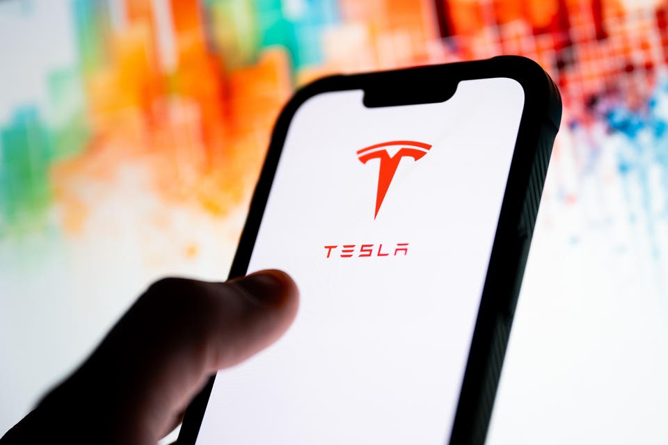 In this photo illustration, a Tesla logo seen displayed on a...