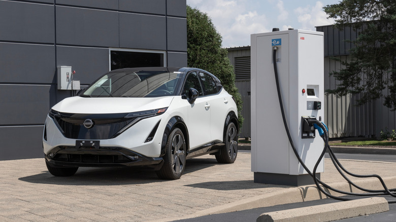 A white 2023 Nissan Ariya next to a charger.