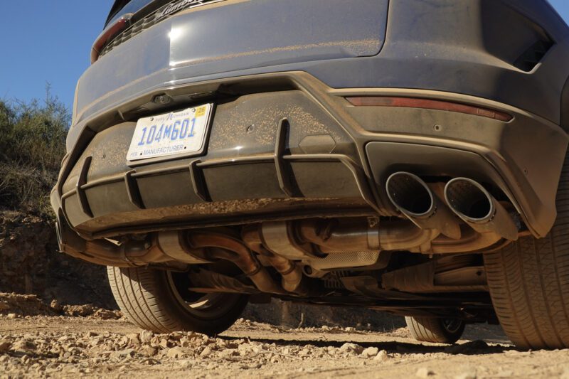 Close-up view of the rear undercarriage of a dusty car on a dirt road, showing the license plate, exhaust pipes, and rear bumper—evoking the rugged power seen in the 2025 Lamborghini Urus SE Review: Heavy Hitter Delivers Plug-In Hybrid Punch.