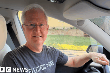 Geoff Perlman Geoff Perlman, with white hair and glasses, sits behind the wheel of a Tesla