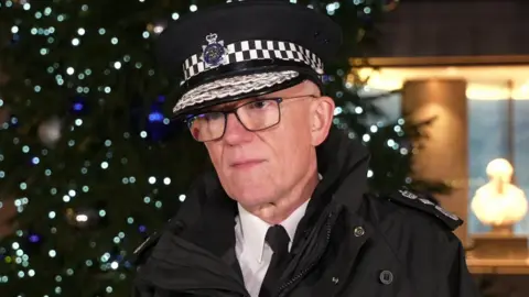 BBC Sir Mark Rowley in uniform outside New Scotland Yard in London. Behind him is an illuminated Christmas tree. 