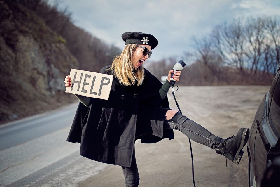 Angry woman is kicking her electric car with empty battery and looking for help