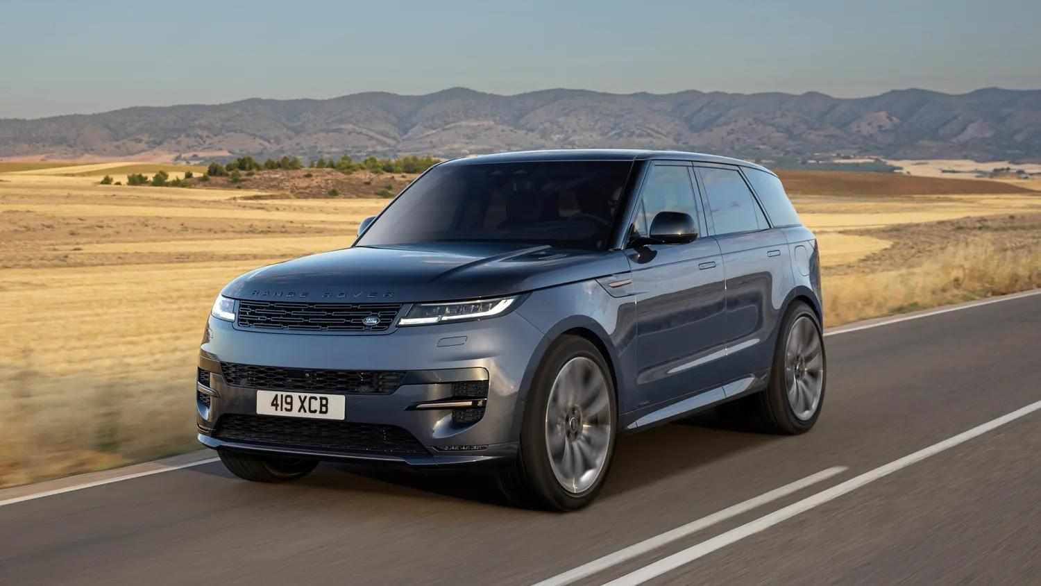 A grey Range Rover Sport driving on a road with a hilly backdrop.