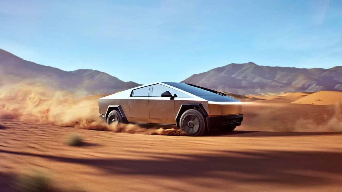 Tesla Cybertruck driving off-road through desert sand dunes, stainless steel electric truck demonstrating high-performance off-road capability