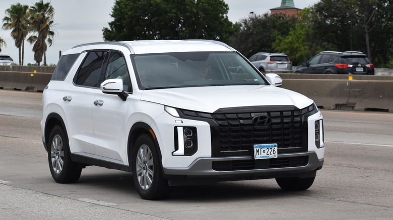 A portrait of a white Hyundai Palisade SE traveling down a highway in moderate traffic