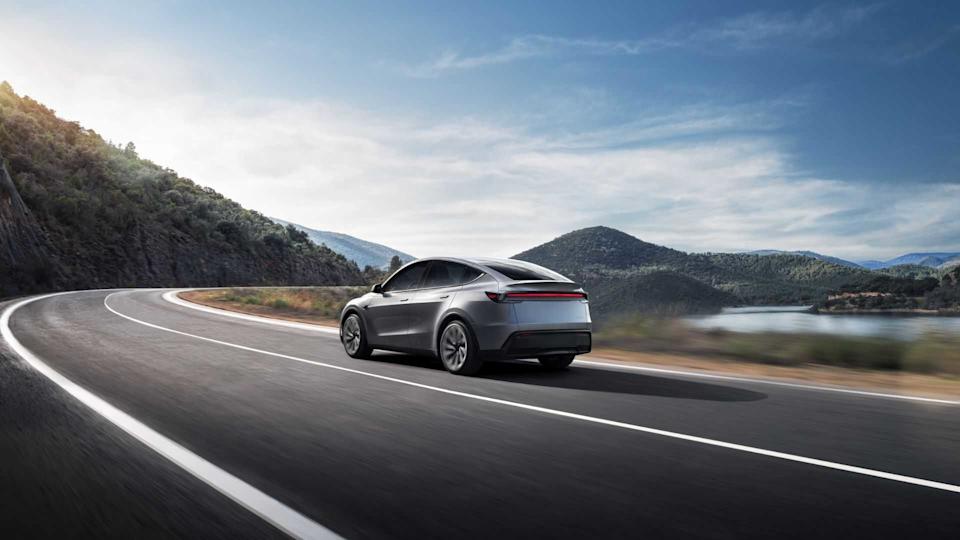 Dynamic rear 3/4 shot of a gray new Tesla Model Y driving on a country road beside a lake.
