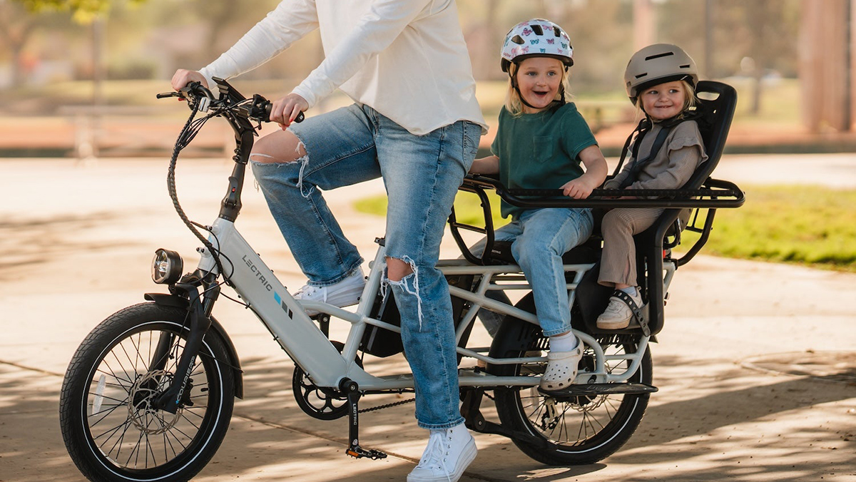 A woman riding a bicycle with two children