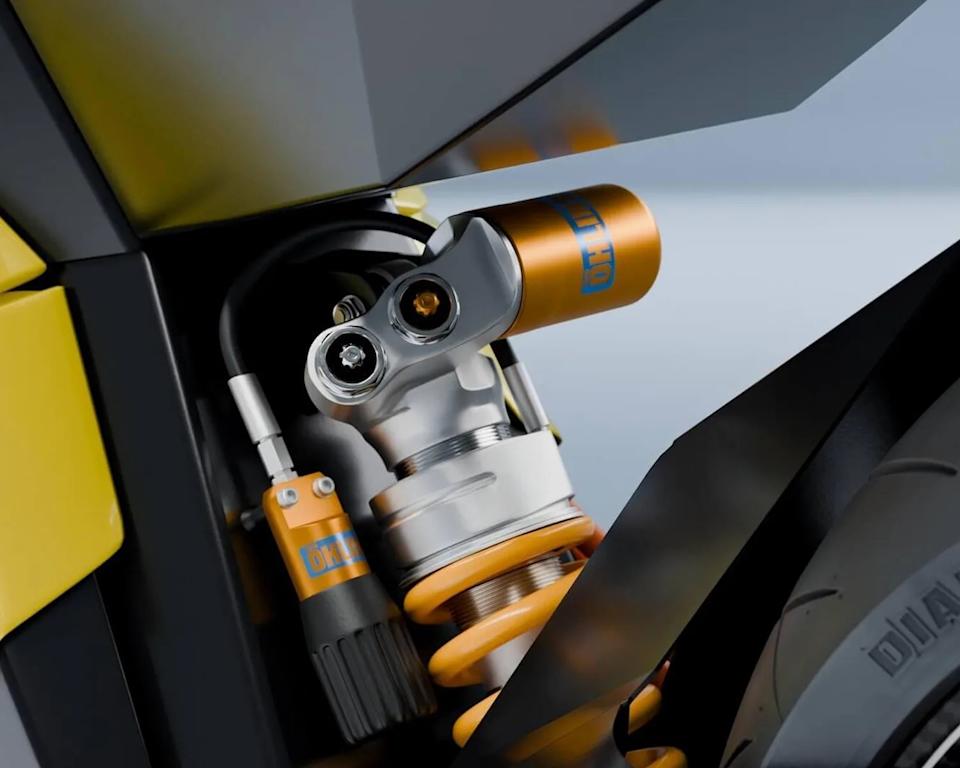 Close-up of a yellow and silver Öhlins motorcycle shock absorber with coil spring near a black tire.