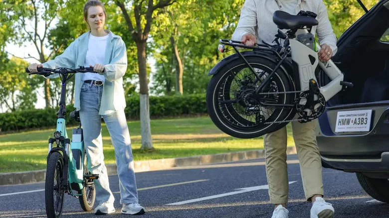 A woman standing beside a Himiway B3 e-bike, a man putting a folded one in the trunk.