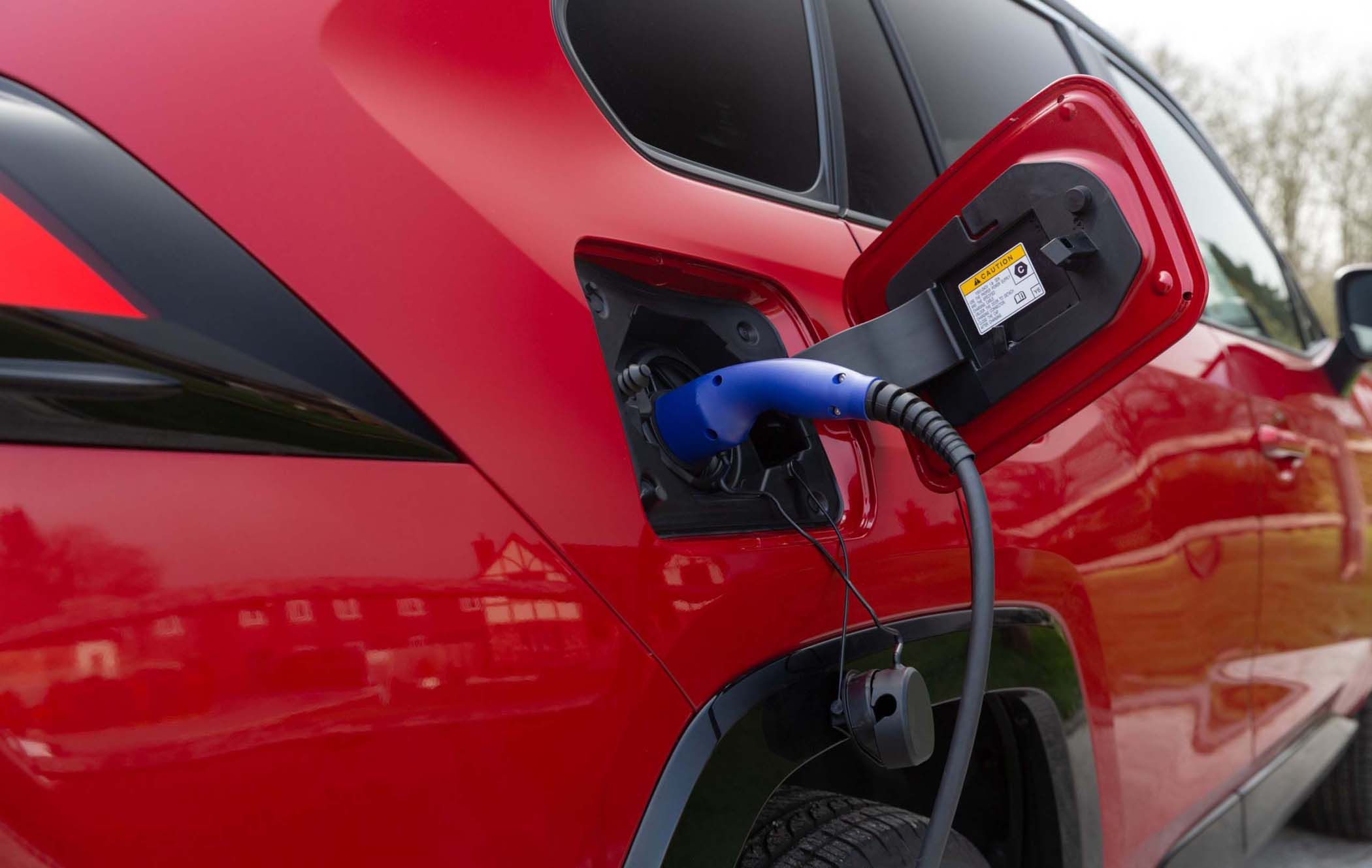 Red Toyota RAV4 being charged with a blue charging cable, connected to the vehicle's charging port, located on the rear side of the car.