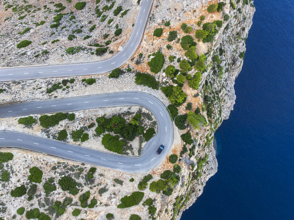Drone picture of a car on harpin bend above the cliff by the sea, Cap de Formentor peninsula, Sierra de Tramuntana, Pollenca, Mallorca, Balearic Islands, Mediterranean Sea, Spain