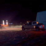 Screenshot from a video showing a Tesla Cybertruck towing an F-350 truck plus a large camping trailer out of deep sand.