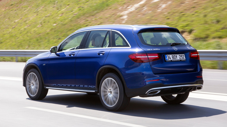 A blue Mercedes-Benz GLC 350e driving on a highway near green hills.