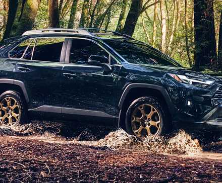 A blue 2024 Toyota RAV4 Hybrid Woodland Edition is driving off-road. 