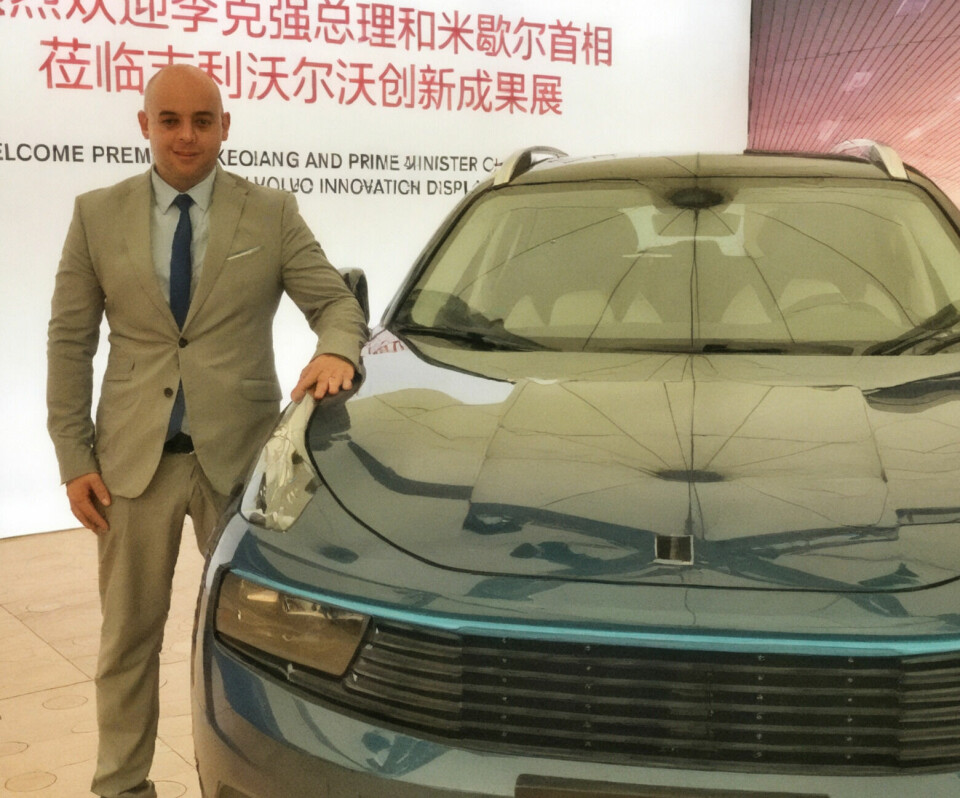 Ash Sutcliffe, global communications chief, Geely Man in a suit stands beside a blue Lynk & Co 01 SUV in an indoor display area.