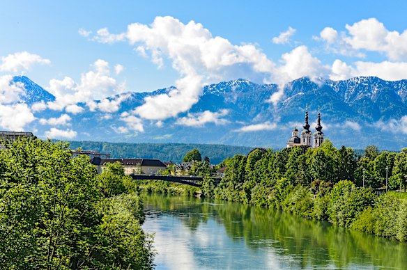 The city of Villach is framed by ethereal mountains and places of worship alongside the Drau River.
