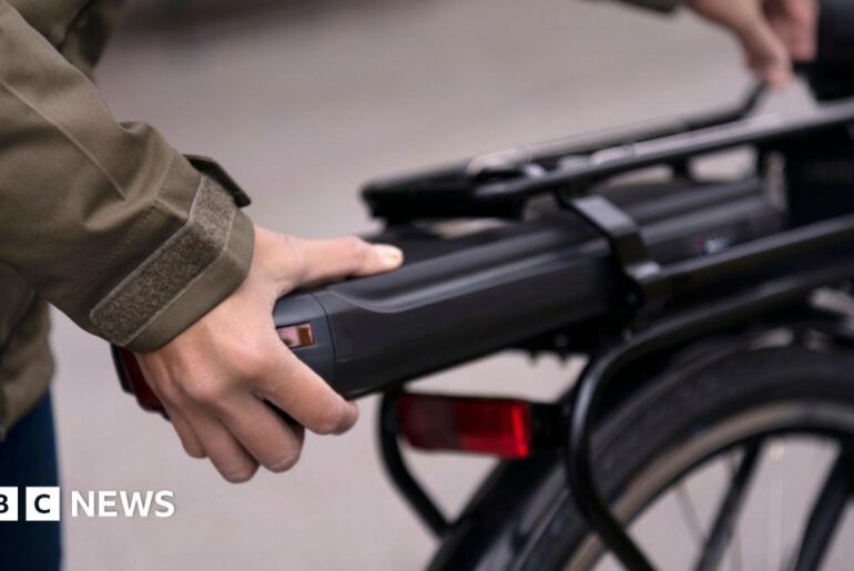 A person changing the battery on the back of an electric bike
