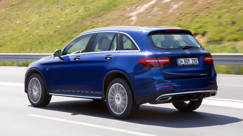 A blue Mercedes-Benz GLC 350e driving on a highway near green hills.