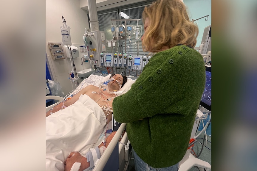 Xavier Sedger lying in a hospital bed with tubes in his nose. He wears a hospital gown.