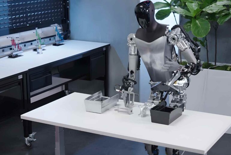 Tesla’s Optimus humanoid robot works at a lab table during a demo, showing AI-driven hands handling small parts.