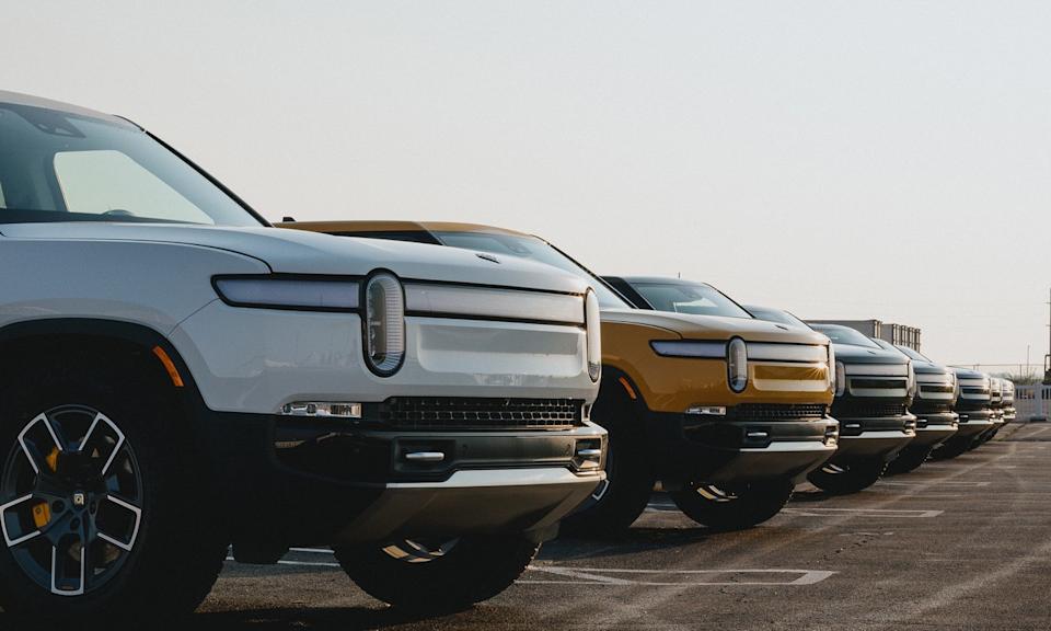 A line of Rivian trucks in a parking lot.