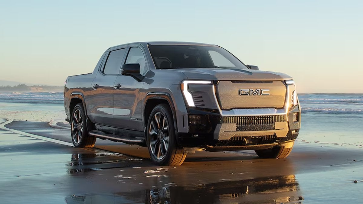 GMC Sierra EV electric truck driving along a beach at sunset, highlighting premium styling, electric power, and coastal scenery.