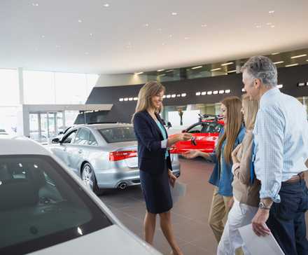 Salesperson in a dealership showroom handing a family keys to a new car.