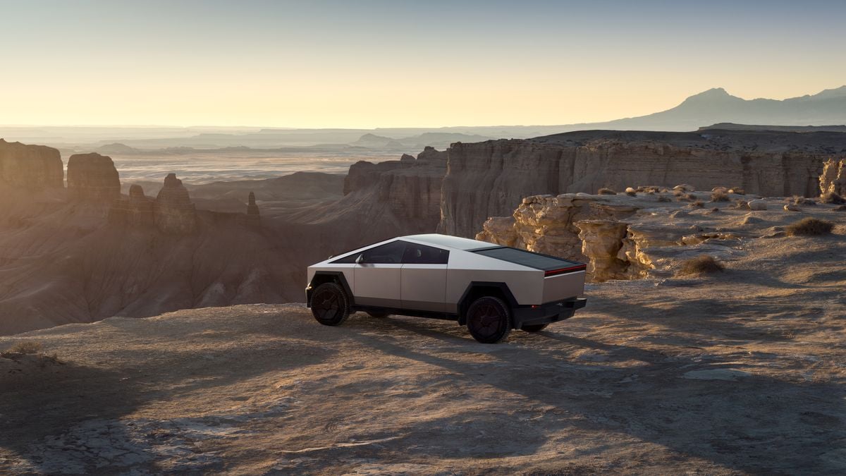 Tesla Cybertruck in stainless steel parked on a desert cliff overlooking a canyon at sunset, showcasing its futuristic electric pickup design and off-road capability.