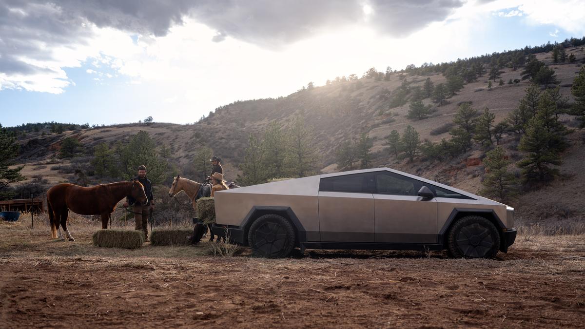 Tesla Cybertruck on a rural ranch beside horses and hay bales, highlighting its rugged stainless steel exterior and utility for farm and work environments.