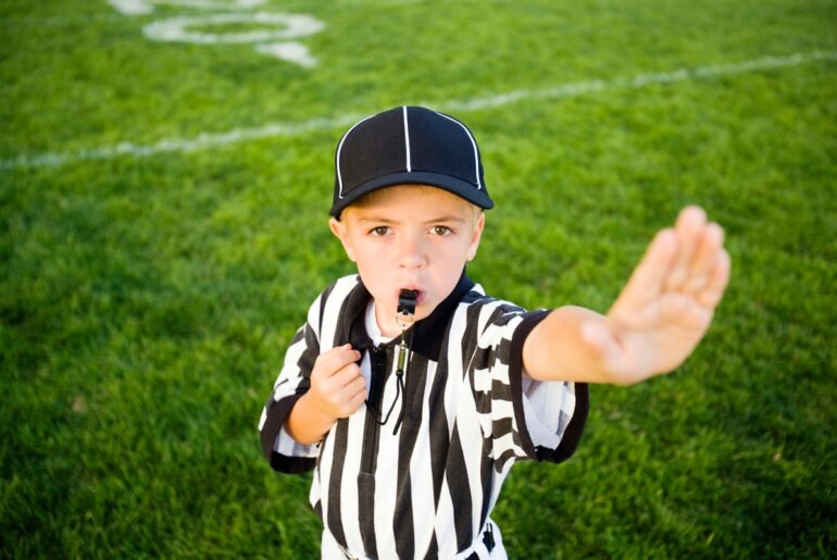 A child in a referee uniform putting his hand up to say stop.