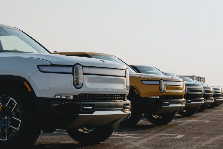 A line of Rivian trucks in a parking lot.