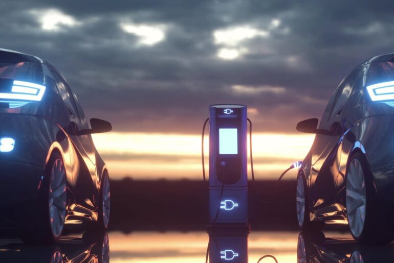 Two electric vehicles charge at a charging station at dusk.