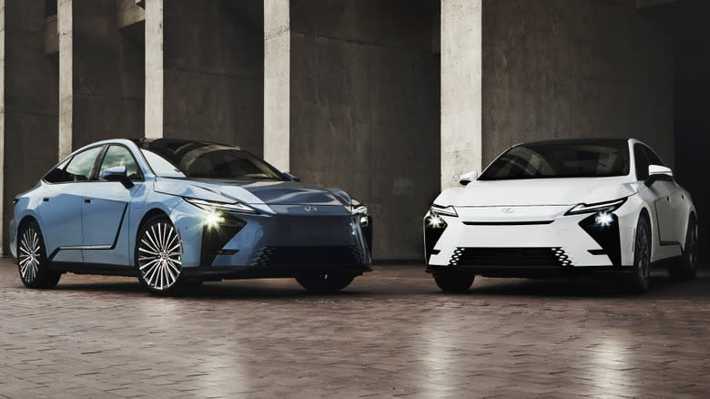 A front three quarter shot of a blue ES EV and a white ES Hybrid parked nose toward eachother on brick in front of concrete pillars