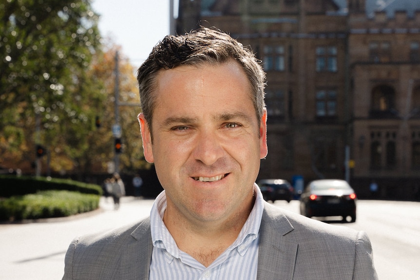 A man in a grey suit smiles at the camera.
