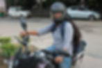 A young woman wearing a three-fourth shirt and jeans rides a gear motorbike. Her helmet carries the logo of Uber Moto.