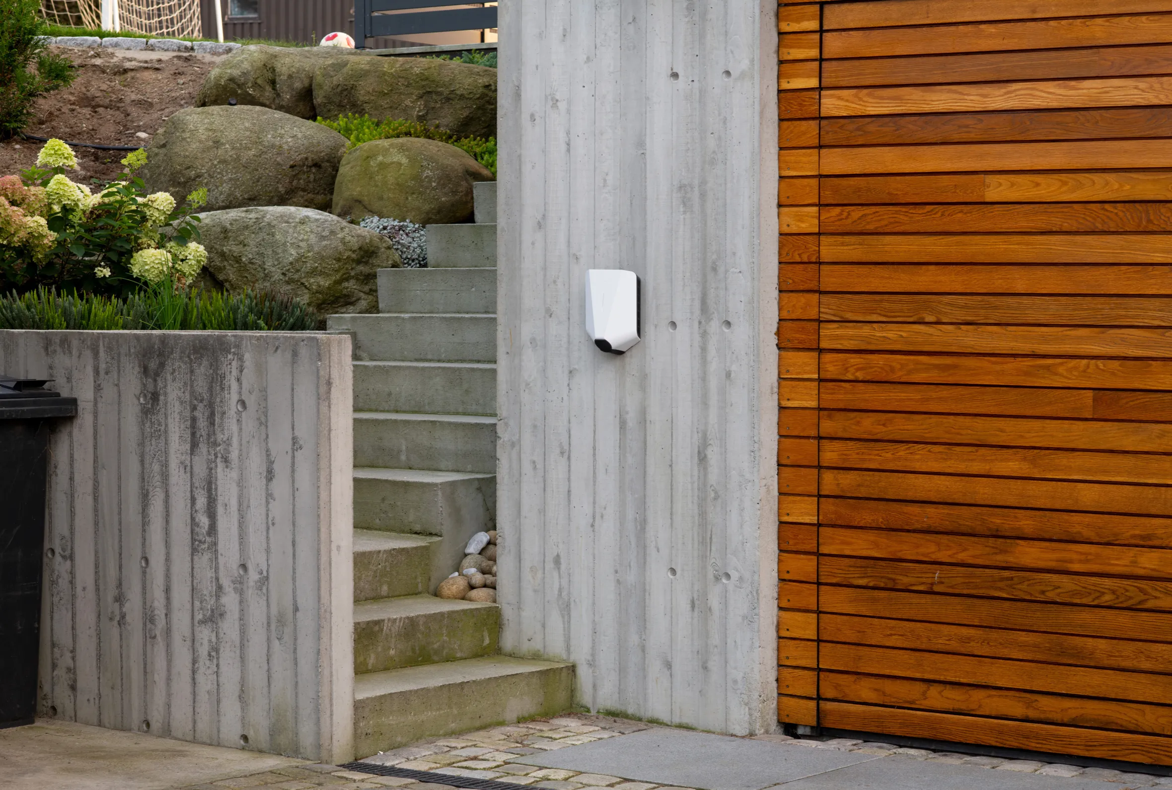 Easee electric car charger mounted on a concrete wall next to a wooden slatted garage door.