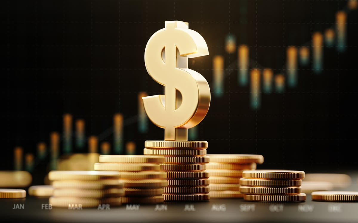 A giant golden dollar sign on top of stacks of golden coins, in front of a stock chart.