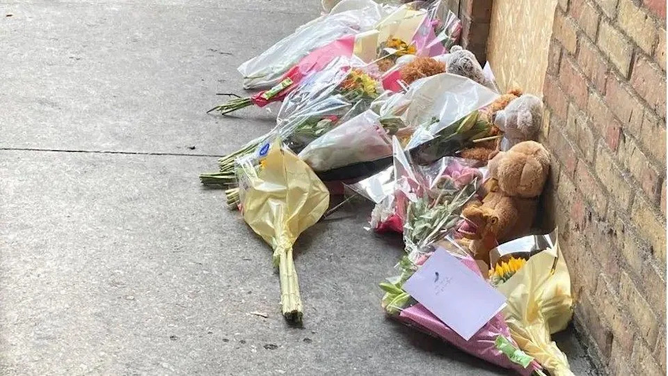 Flowers and teddy bears and lined up next to a wall on the right hand side. They are lying on a concrete floor.