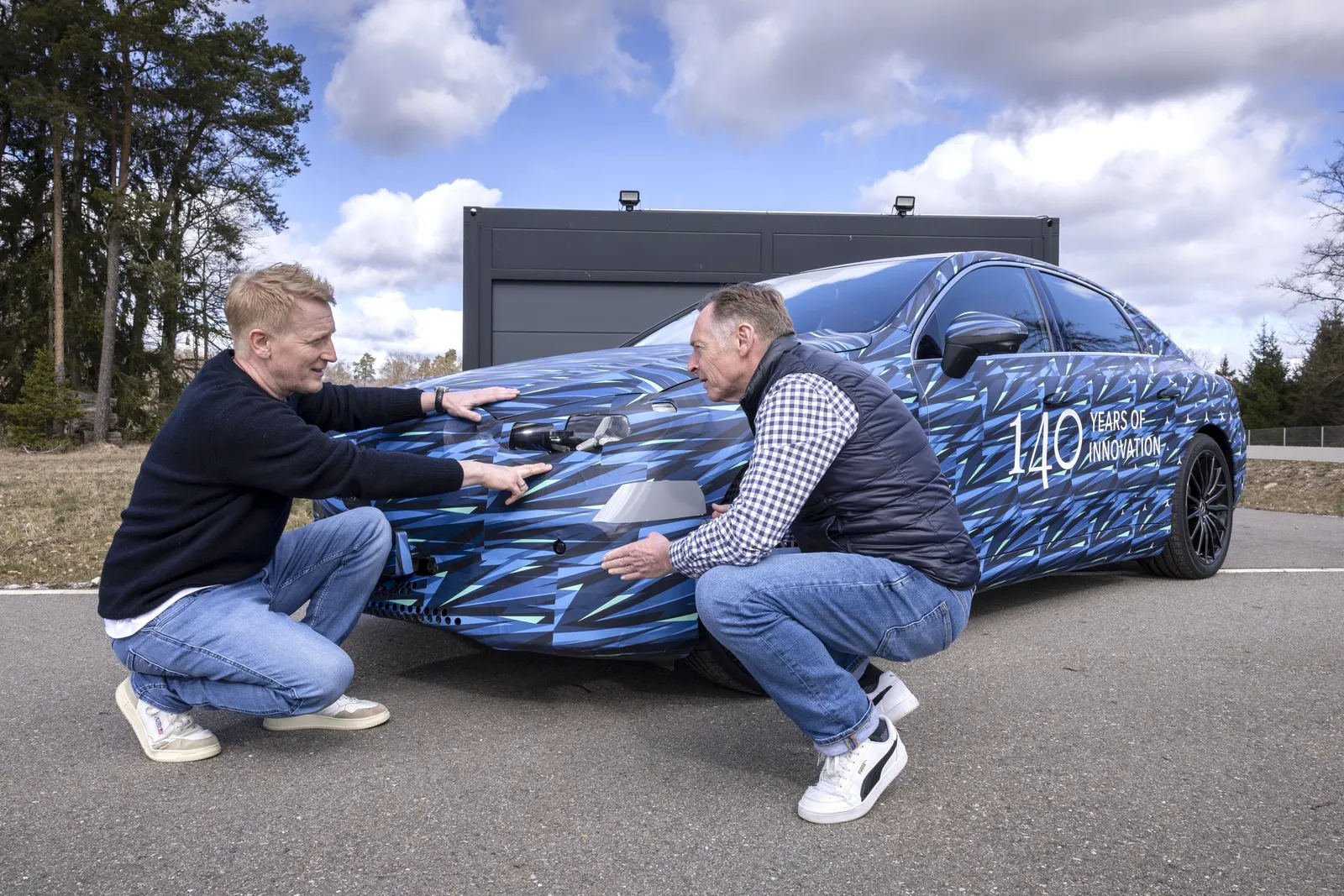 Mercedes ride engineer Ewald Dirks crouches at the front of the C-Class Electric prototype with Greg Kable
