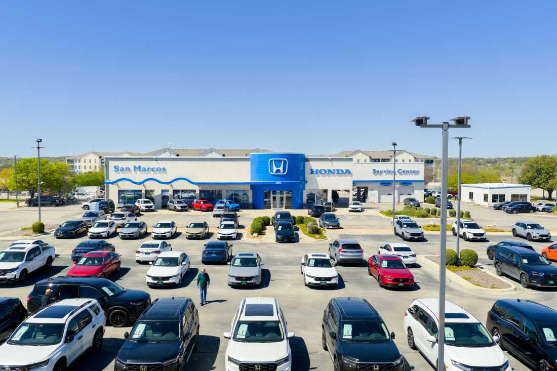 A person walks across a lot full of parked vehicles at a Honda dealership.