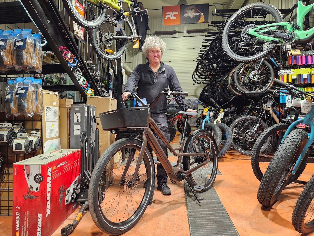 A man holds a bike in a store, surrounded by other bikes.