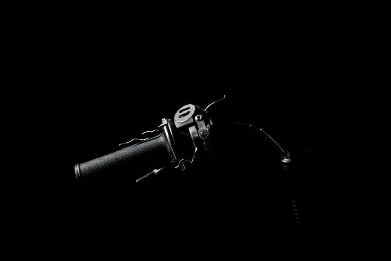 An extreme close-up photograph of a damaged e-moto or pocket bike part, such as a broken handlebar or cracked frame, lit by a harsh, direct camera flash against a pitch-black background, conceptually illustrating the aftermath of a street takeover incident.