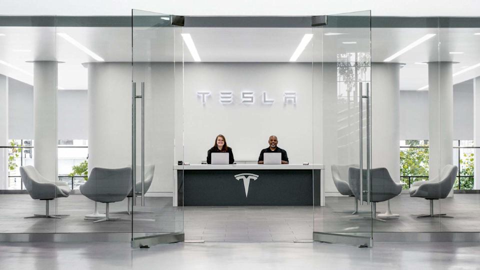 Two employees sat at desk welcoming customer to a Tesla car showroom