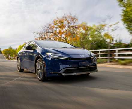 Front 3/4 view of a navy blue 2025 Toyota Prius driving on a country road.