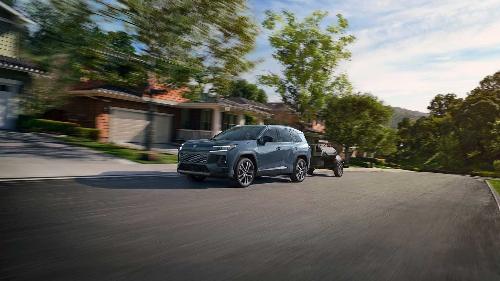 Dynamic front 3/4 shot of a blue 2026 Toyota RAV4 Limited towing a trailer through a residential area.