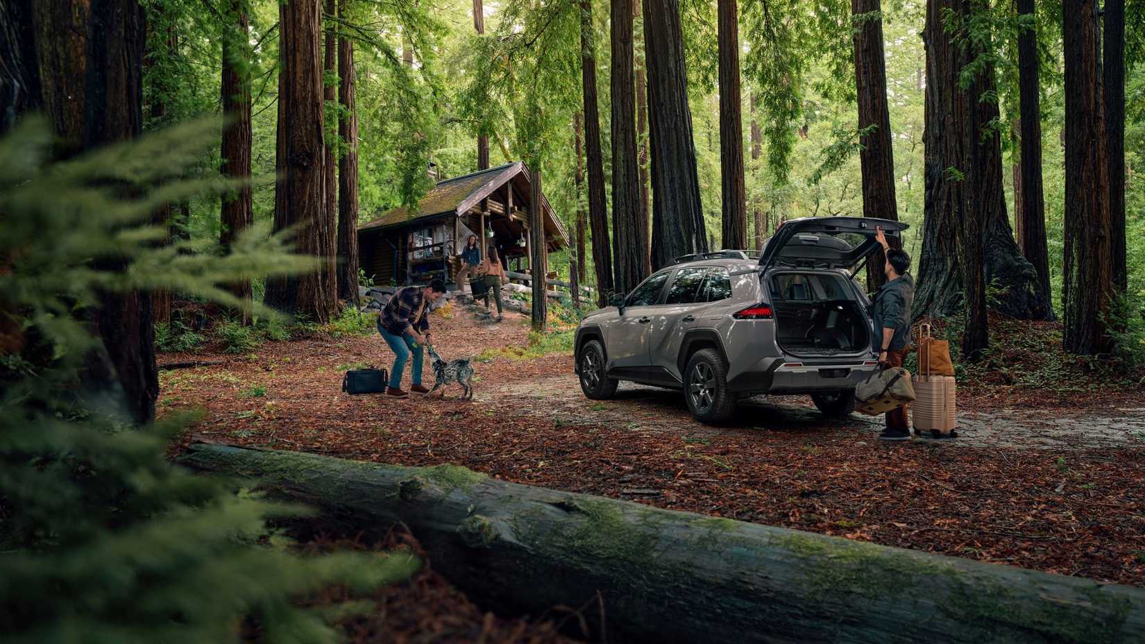 Static rear 3/4 shot of a gray 2026 Toyota RAV4 Woodland parked in a forest with a person open its trunk.