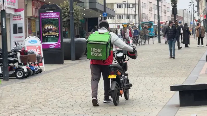 Man with green uber eats food delivery backpack walking through city centre pushing bike