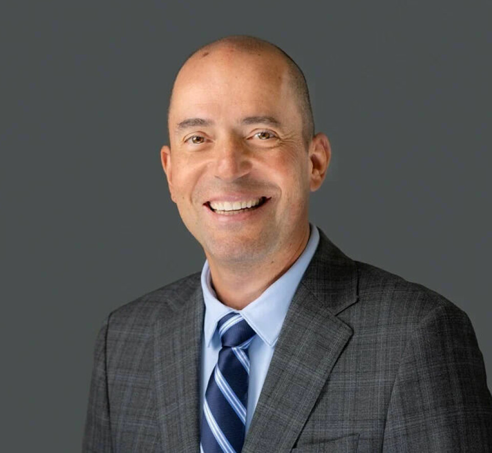 Smiling suited man in a tie posing against a plain grey studio background.