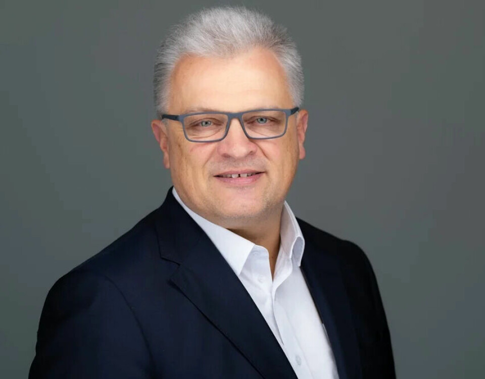 Middle-aged man in glasses and suit jacket posing against a plain grey background.